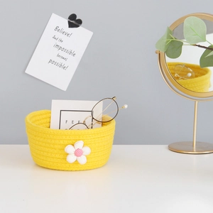 Detail of yellow cotton rope woven storage basket with white flower decor on a desk