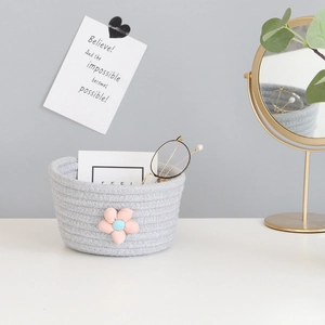 Detail of grey woven cotton rope storage basket featuring a decorative pink fabric flower