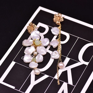 Detailed close-up of asymmetric gold floral earrings with baroque pearls and long tassels