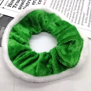 Close-up of green velvet Christmas scrunchie with white plush trim on newspaper background