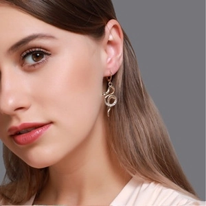 Gros plan de boucles d'oreilles serpent dorées avec zircons portées par un modèle