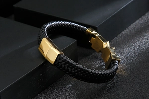 Detail of black braided leather bracelet with a polished gold cross metal clasp