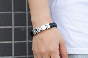 Macro shot of men's black braided leather bracelet with silver crystal X magnetic clasp