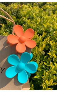 Detail of matte flower hair claws in orange and teal on a paper bag outdoors