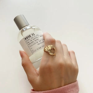 Detail of a gold irregular textured lava ring worn on a finger with a luxury bottle