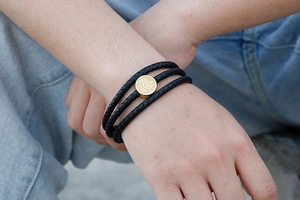 Detail of multi-layer braided leather bracelet with golden charm showing '忍' engraving