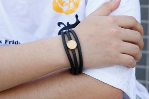 Detail of multi-layer braided black leather bracelet with a gold-tone round metal charm