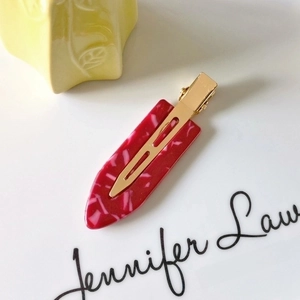 Detail of red marble texture hair clip with golden metal alligator buckle on white background