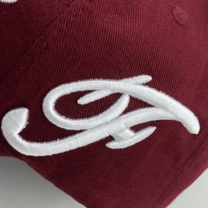 Detailed macro view of white embroidery on a wine red cotton baseball cap fabric