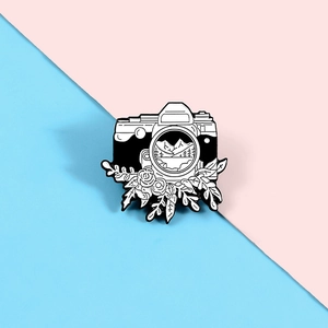 Detailed view of a vintage camera enamel pin with floral and landscape illustrations