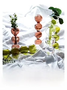 Détail de vases sphériques empilés en verre ambre et vert sur un tissu texturé blanc