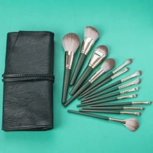 Detail of 12-piece dark green makeup brush set with gray bristles and black leather wrap