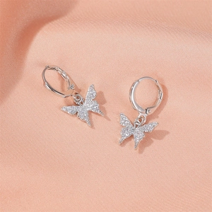 Détail de boucles d'oreilles papillon en argent avec zircons sur fond de soie