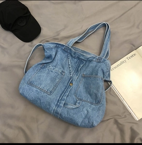 Detail shot of blue denim tote bag featuring two front pockets and metal button accents
