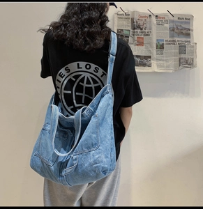 Detail of blue denim tote bag with wide strap and external pocket on casual street style model