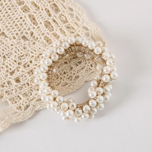 Detailed close-up of high-elasticity golden woven hair tie with shiny white pearls