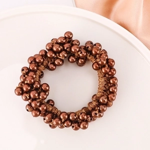 Brown beaded elastic hair tie with metallic finish pearls on a white tray background