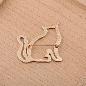 Golden cat brooch featuring a hollow silhouette design and a pin back on wood background