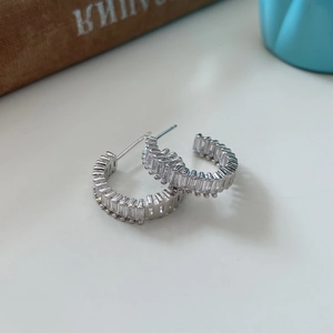 Detailed shot of silver C-shaped earrings with rectangular cubic zirconia on a desk