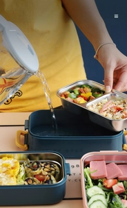 Close-up showing hot water being poured into the base of the double-layer lunch box for warmth