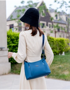 Outdoor shot of a blue oxford crossbody bag worn by a model against a villa background