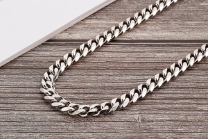 Detailed macro view of a polished silver Cuban link body chain on a wooden surface