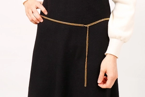 Detail view of a slim gold NK chain waist belt on a black dress with adjustable clasp