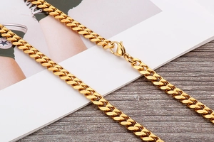 Detail of a polished golden Cuban link chain with a secure lobster clasp on wood background