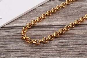 Close-up of golden pearl body chain with sleek Rollo links on dark wood background