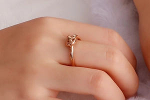 Close-up of rose gold knot ring worn on a finger with soft white plush background