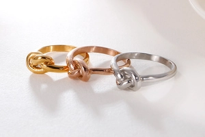 Detailed view of knot-shaped rings in gold, rose gold, and silver metallic finishes