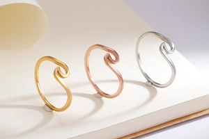 Three wave-shaped stainless steel rings in gold, rose gold, and silver finishes displayed