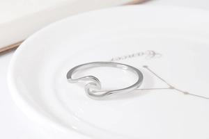 Macro detail of wave shaped minimalist silver ring on a white ceramic plate background
