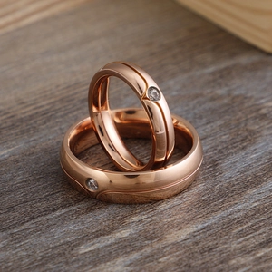 Polished rose gold stainless steel couple rings set with center zircon inlay on wood