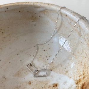 Close-up of interlocking silver rectangles necklace with zircons in a ceramic bowl