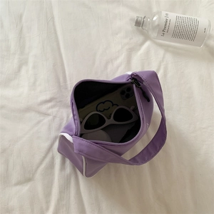 Purple nylon underarm bag on white sheets showing storage capacity for phone and glasses
