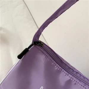 Close-up of purple nylon shoulder bag showing black metal zipper and reinforced stitching