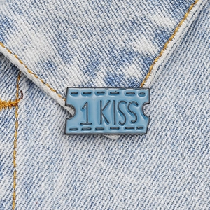 Blue enamel pin with 1 KISS ticket design on light blue denim fabric pocket