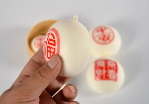 Gros plan d'une main pressant le jouet squishy en forme de brioche avec signe Fu