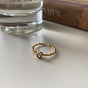 Detail of gold bead ring with zircon stone set against a luxury perfume and book