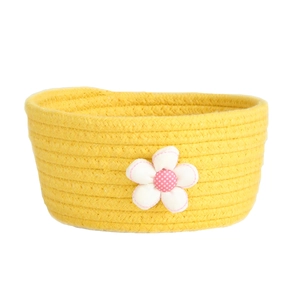 Yellow woven cotton rope storage basket with decorative white flower on white background