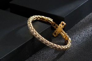 Detailed shot of gold braided stainless steel bracelet featuring a cross charm on black stand