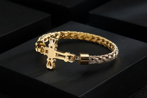 Detail of gold woven chain bracelet featuring a cutout cross and heart shaped charms