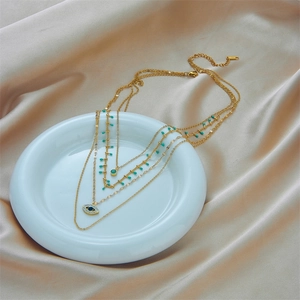 Multi-layer gold chain necklace with turquoise beads and evil eye pendant on silk background