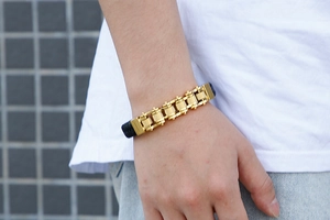 Mechanical gold chain bracelet with black leather base shown on a person wrist