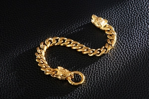 Detail of golden wolf head bracelets with bold curb chain on black leather background
