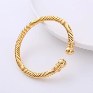 Macro shot of gold-plated twisted cable bracelet featuring round ball ends on white marble