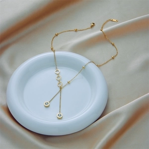 Elegant gold titanium steel necklace with triple rings and zircon tassels on silk background
