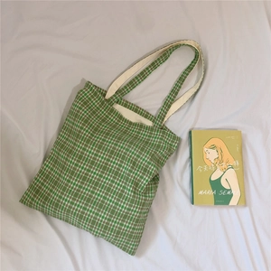 Detail shot of green checkered canvas tote bag with book on natural fabric surface