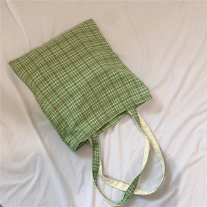Detailed top view of a green and white plaid canvas tote bag on a white fabric surface